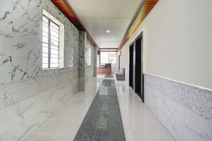 A corridor with marble walls and a wooden ceiling, leading to a reception area with a sofa and a counter. - Hotel O Talegaon MIDC Goodluck Lodge (Pune)