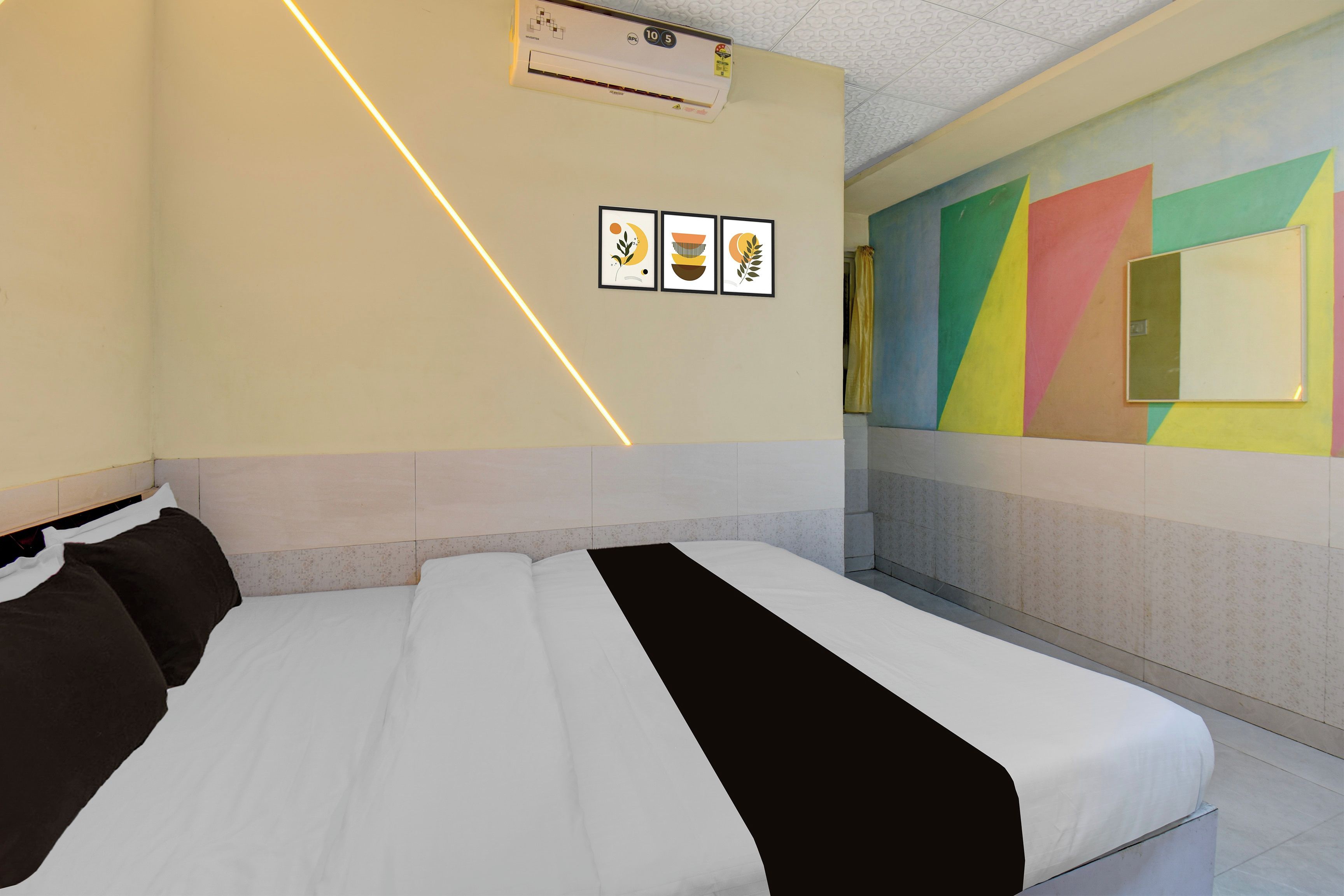 A hotel room with a bed, a wall-mounted air conditioner, and a colorful wall mural.