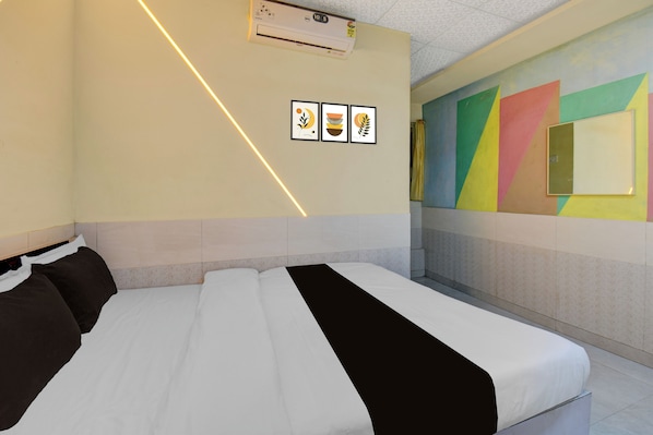 A hotel room with a bed, a wall-mounted air conditioner, and a colorful wall mural.