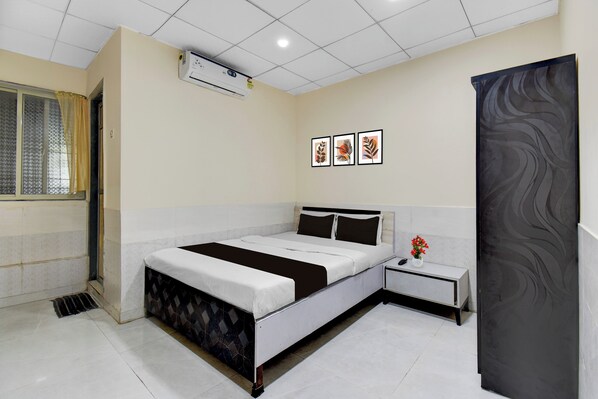 A hotel room with a bed, bedside table, nightstand, and a window with a curtain.