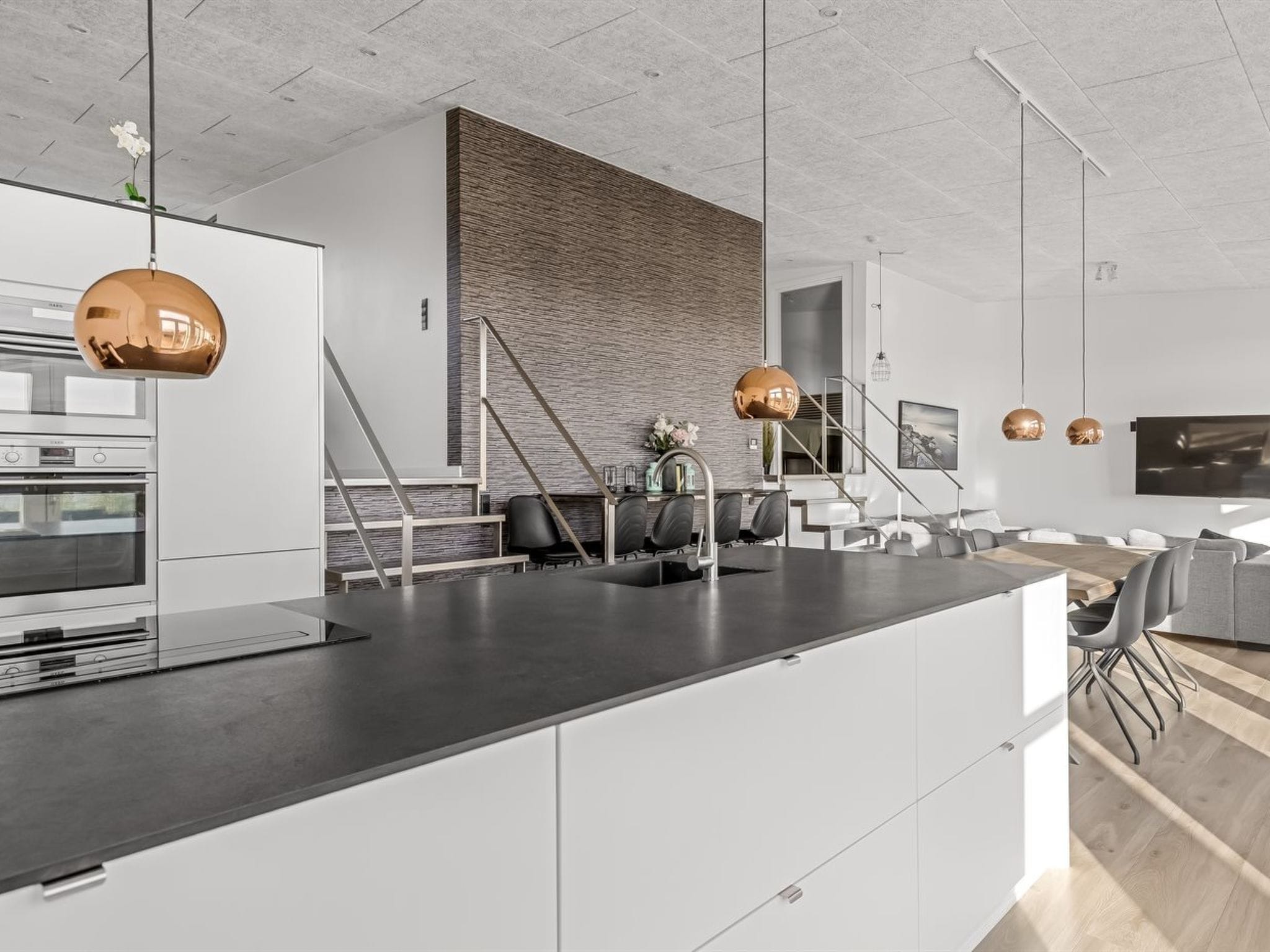 Une cuisine moderne dotée d’un îlot central, d’appareils électroménagers en acier inoxydable et de luminaires suspendus.