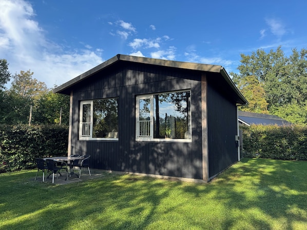 A small, dark wooden cabin with two windows and a patio area with a table and chairs. - Get away from it all together in a completely detached tiny house on the edge of the Drenthe forest in Gasselte. (Gasselte)