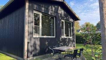 A small wooden building with a balcony, a table, and two chairs.