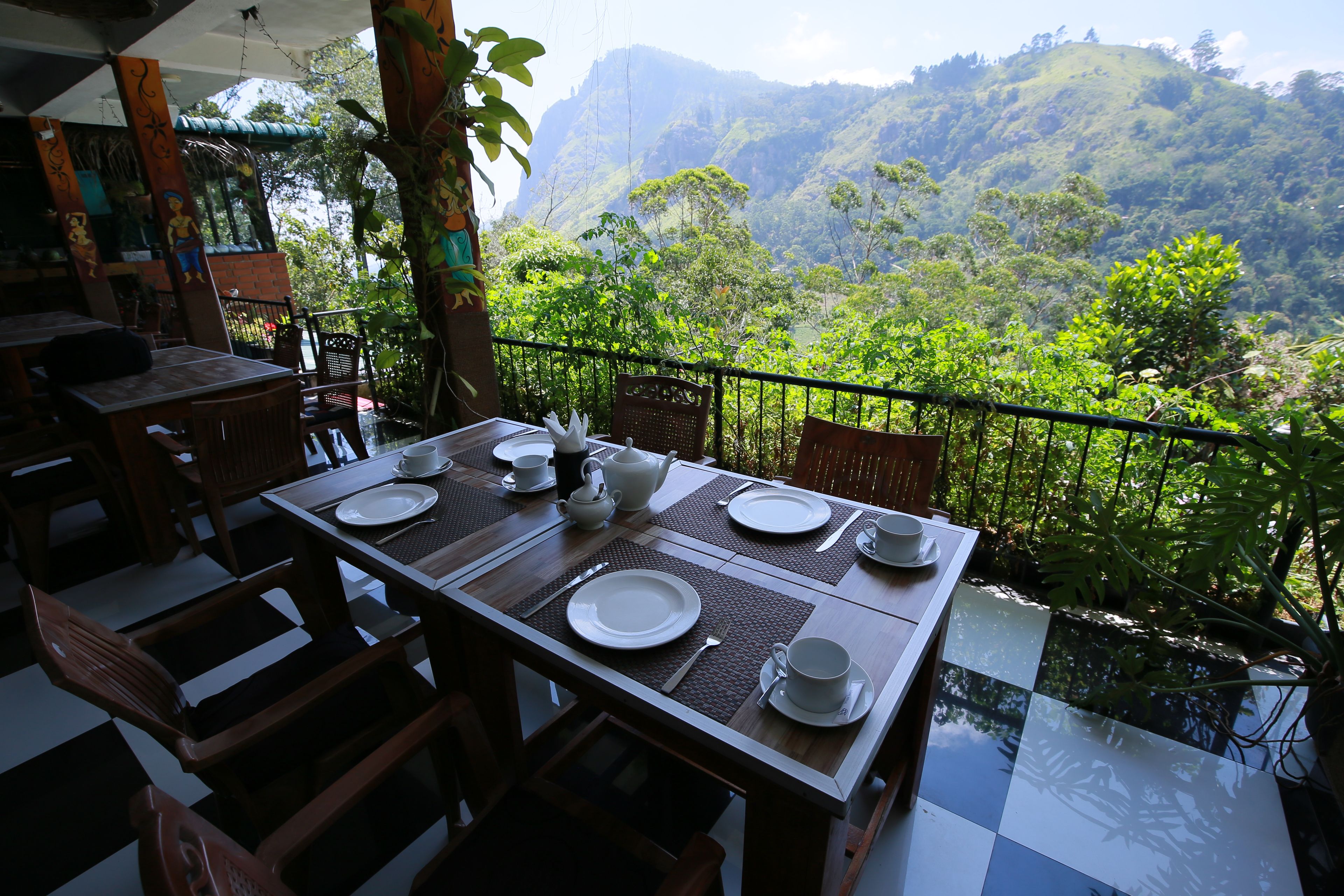 Una mesa de comedor dispuesta con platos, vasos y cubiertos, con vistas a un valle exuberante.