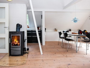A room with a wood-burning stove, a dining table with chairs, and a kitchen area with cabinets and appliances. - 8 Person Holiday Home in Hemmet (Hemmet)
