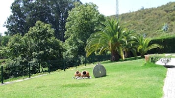 Un espacio con césped, un sendero, árboles y una alta torre de comunicaciones al fondo.