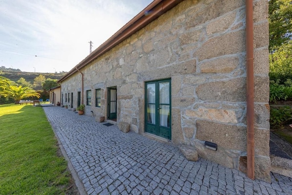 Un edificio de piedra con un camino adoquinado, puertas verdes y un área con césped.