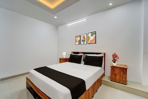 A modern bedroom with a large bed, a bedside table with a lamp, and a nightstand with a vase of flowers. - Hotel O Erumeli Kottayam Pious B (Kottayam)
