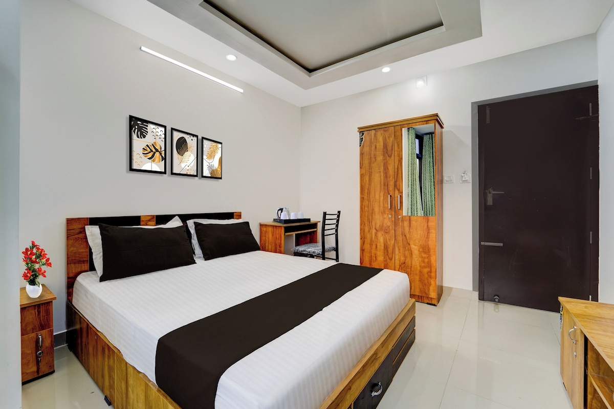 Una habitación de hotel moderna con una cama grande, un armario de madera, una mesita con una silla y una obra de arte enmarcada en la pared.