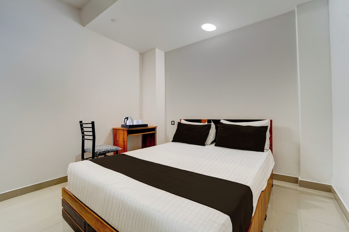 Habitación individual con una cama y cabecera de madera, una mesita de noche con tetera y una silla.