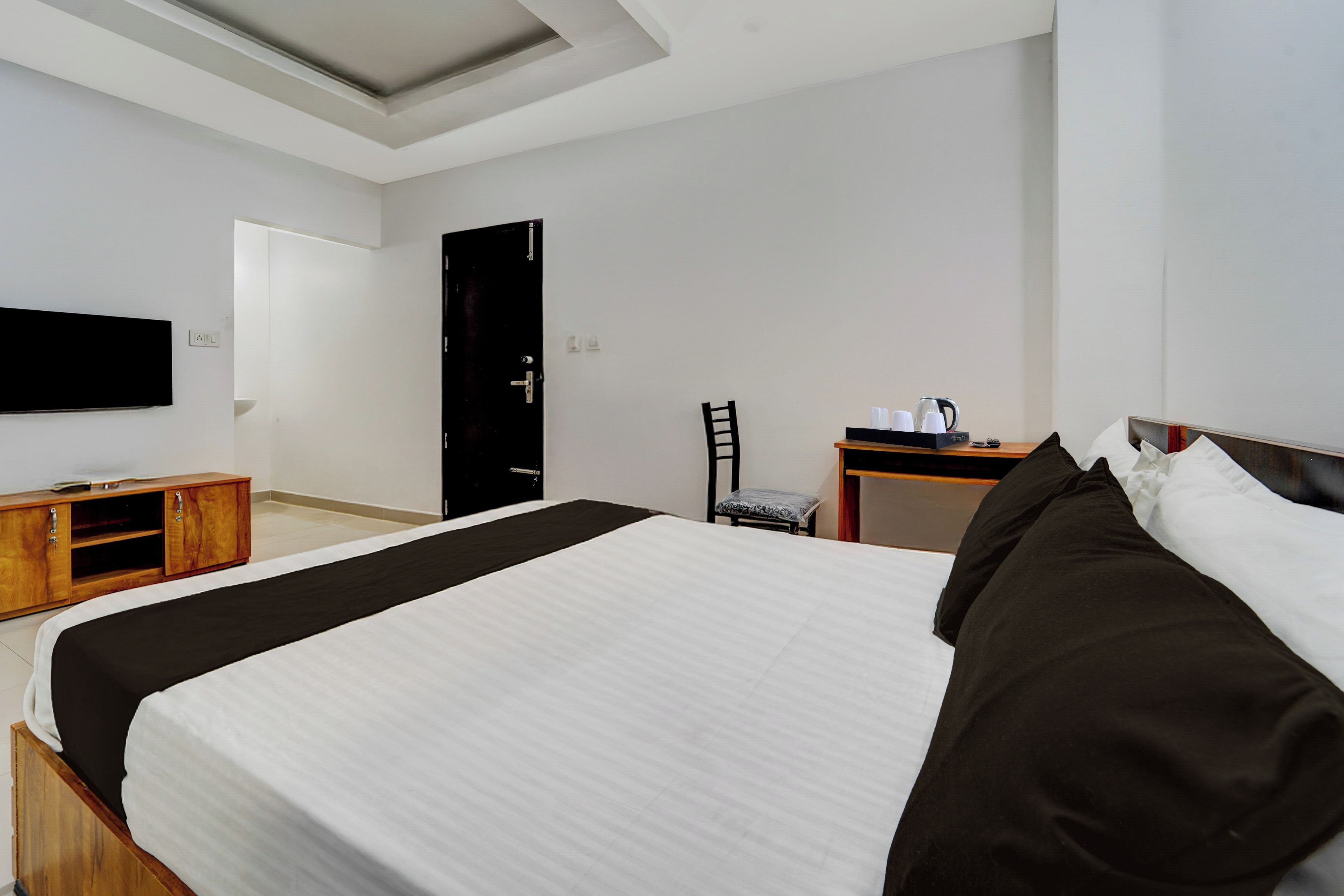 Una habitación de hotel con cama, escritorio, silla y televisor en la pared.