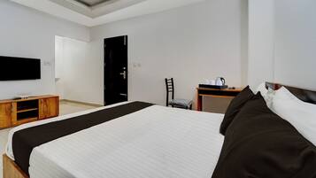 Una habitación de hotel con cama, escritorio, silla y televisor en la pared.