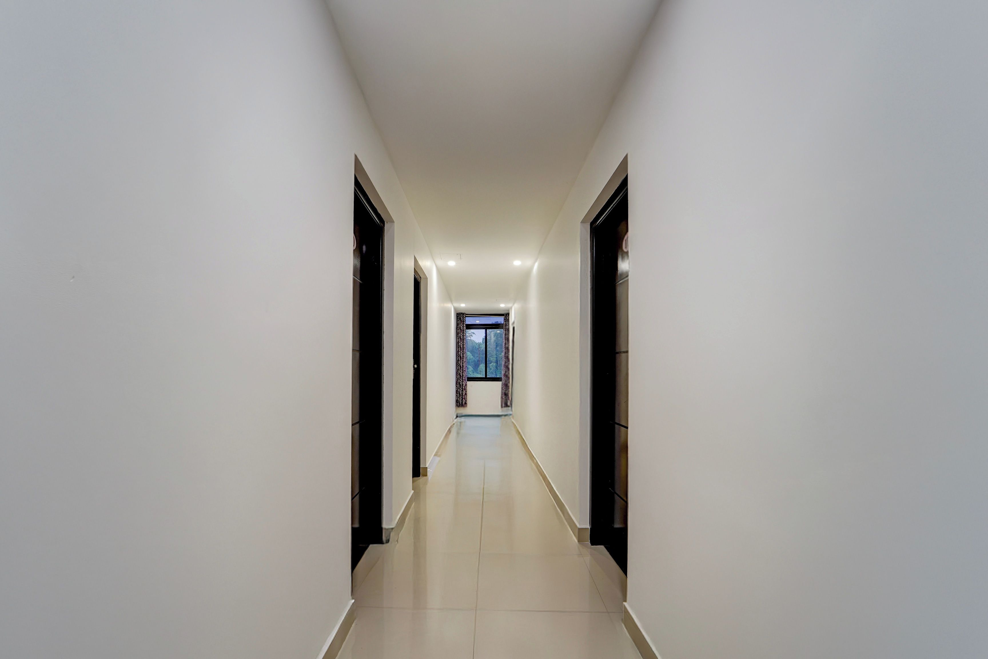 Un pasillo largo y estrecho con piso de baldosas y paredes blancas, que conduce a una habitación con ventana.