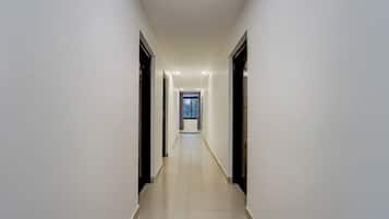 Un pasillo largo y estrecho con piso de baldosas y paredes blancas, que conduce a una habitación con ventana.