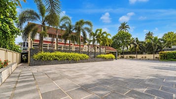 A spacious outdoor area with a paved walkway, palm trees, and a building with a red roof.