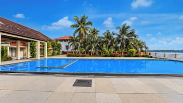 Ein Swimmingpool mit einer gefliesten Terrasse, umgeben von Palmen und einem Gebäude mit einem Ziegeldach.