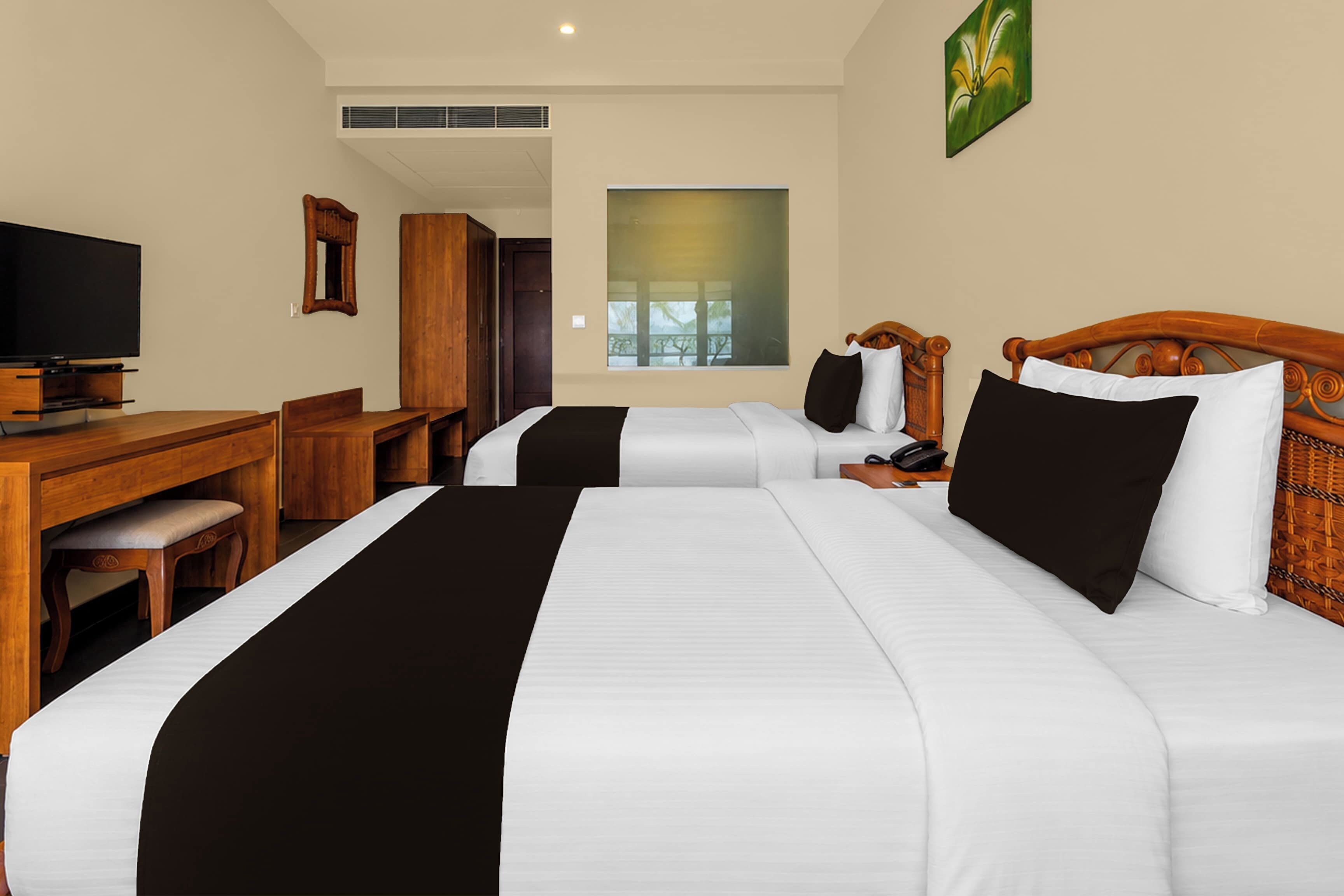 A hotel room with two beds, a desk, a television, and a window.