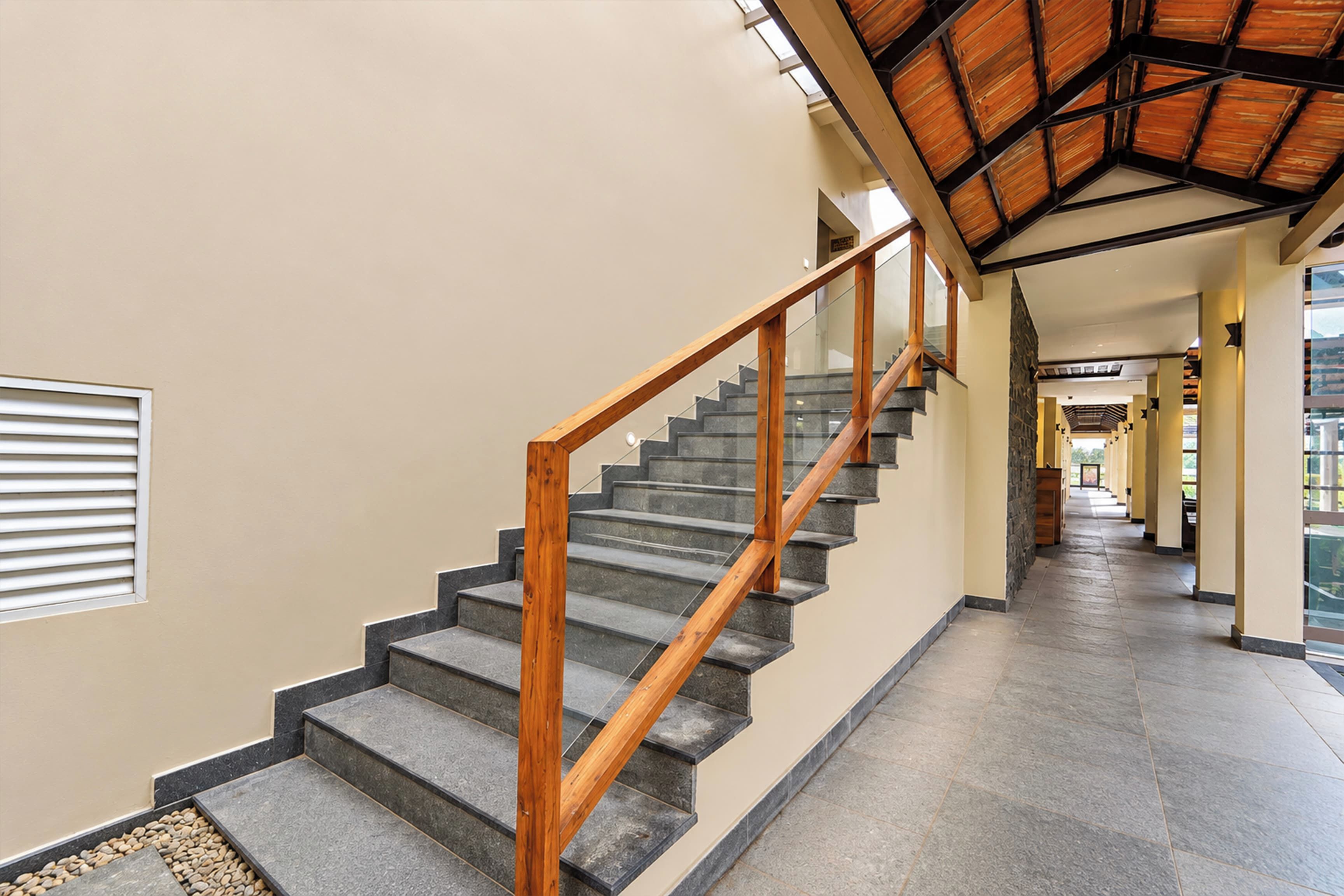 A staircase with wooden handrails and stone steps, leading to a covered area with a high ceiling.