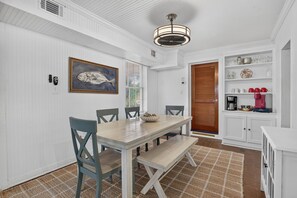 Ein Essbereich mit Holztisch und Stühlen, einem Deckenventilator und einer Küchenzeile mit Regalen und Geräten.