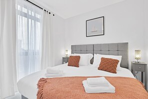 Ein modernes Schlafzimmer mit einem großen Bett, zwei Nachttischen, einer Kopfteil und einem gerahmten Bild an der Wand.