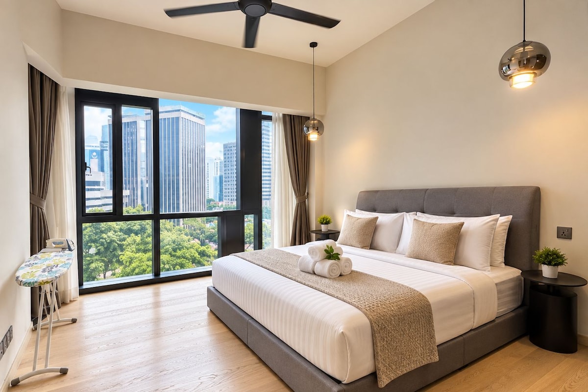 A modern bedroom with a large bed, a standing fan, a small table with a plant, and a view of the city through large windows.