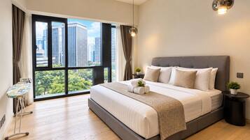 A modern bedroom with a large bed, a standing fan, a small table with a plant, and a view of the city through large windows.