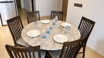 A round marble dining table with six chairs, surrounded by white plates and clear water bottles.