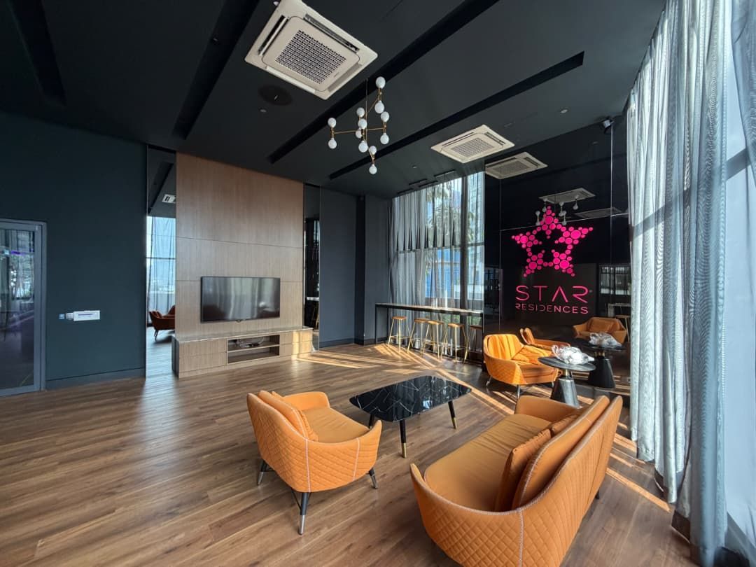 Un área de estar moderna con un televisor grande, asientos cómodos y un letrero visible de 'STAR RESIDENCES'.