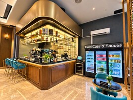 Zona de bar con barra curva, asientos y un mostrador refrigerado con embutidos y salsas.