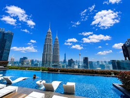 Piscina en la azotea con sillones de descanso, cielo azul despejado y las Torres Petronas al fondo.