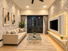 A modern living room with a sofa, a glass coffee table, and a large TV mounted on a textured wall.