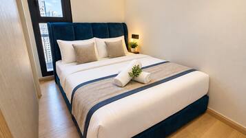 Una cama bien hecha con cabecera azul, ropa de cama blanca y una pequeña planta sobre la cama.