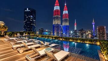 A rooftop pool area with lounge chairs and a city skyline in the background.
