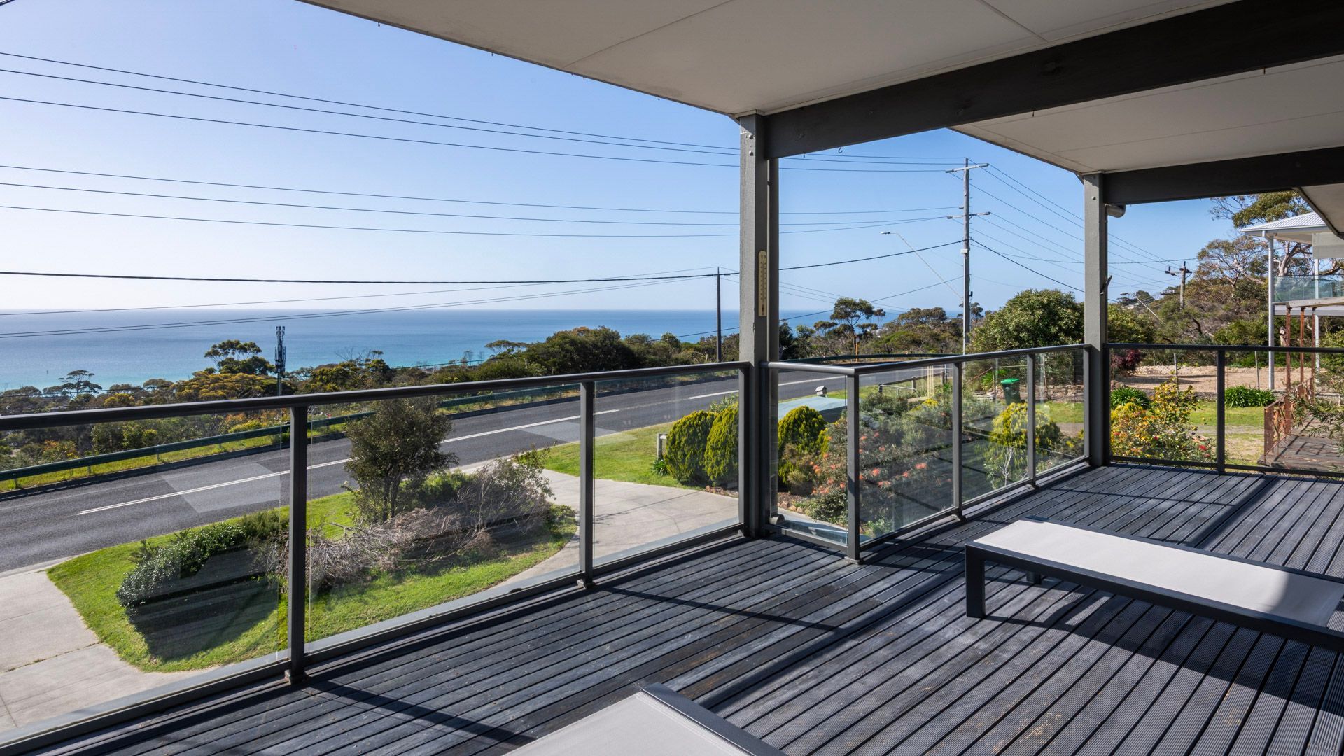 A balcony with a view of a road and greenery, a clear sky, and a distant body of water.