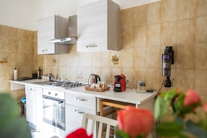 Une cuisine moderne avec des meubles blancs, une cuisinière à gaz, une machine à café et une bouilloire.