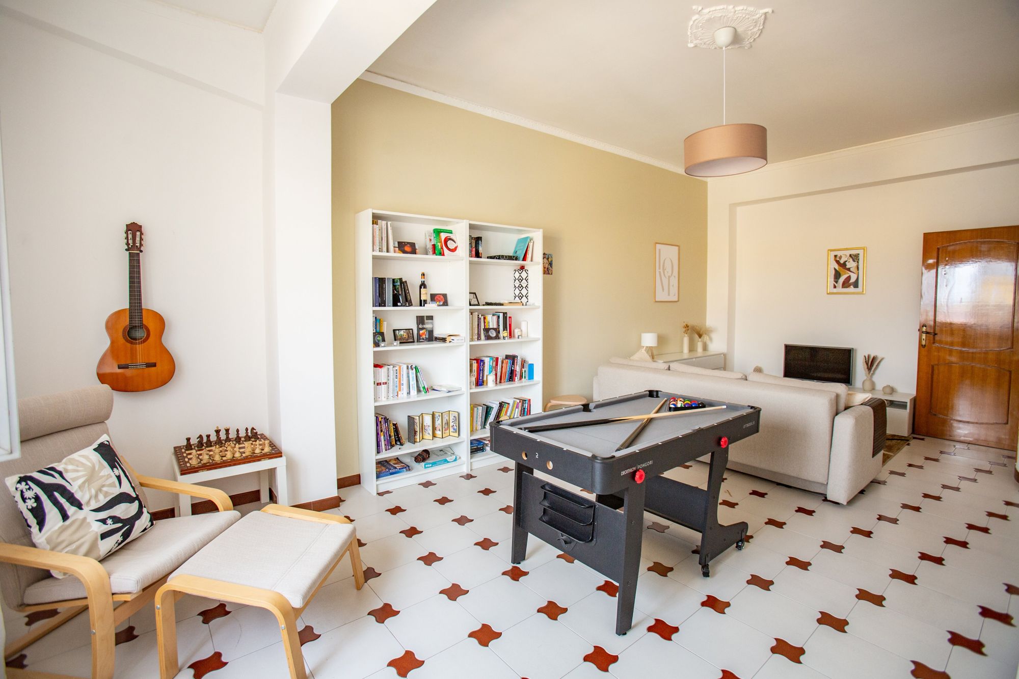 Een woonkamer met een pooltafel, een boekenkast, een bank, een salontafel en een gitaar.