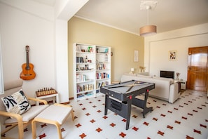 A living room with a pool table, a bookshelf, a sofa, a coffee table, and a guitar.