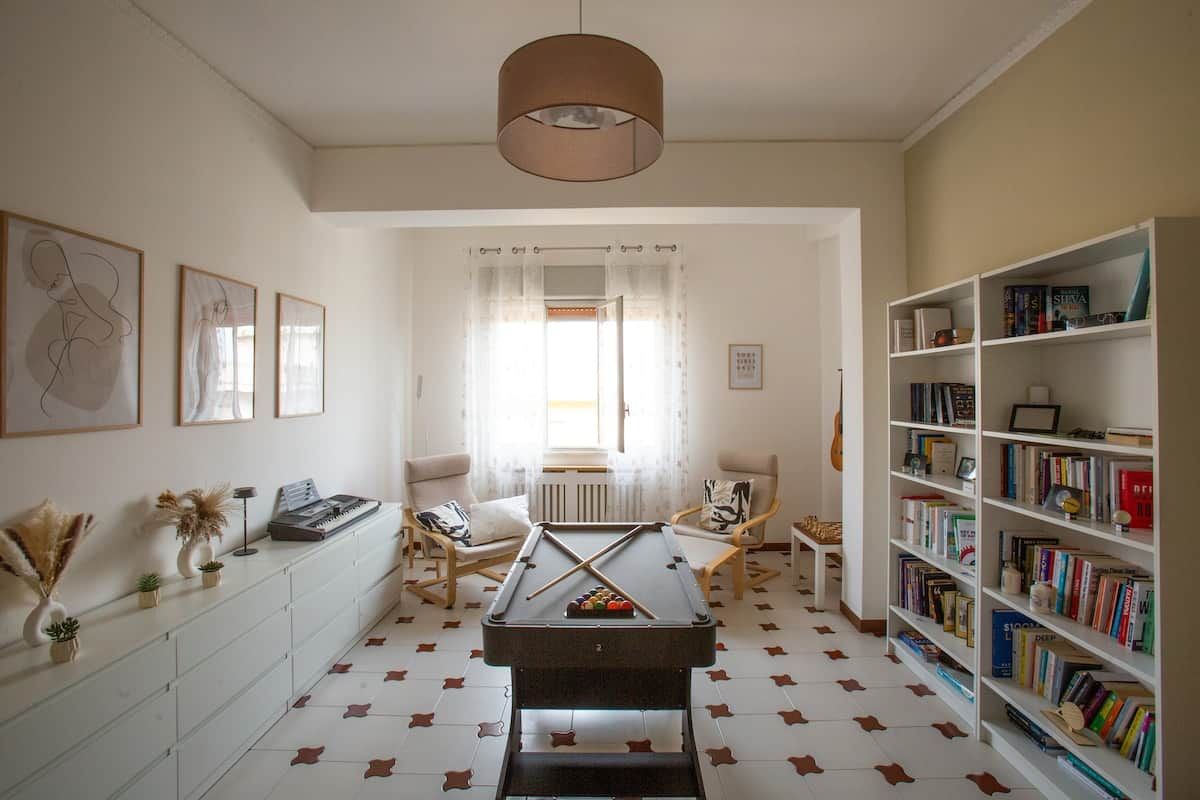 Una habitación con mesa de billar, estanterías y un ventanal con cortinas.