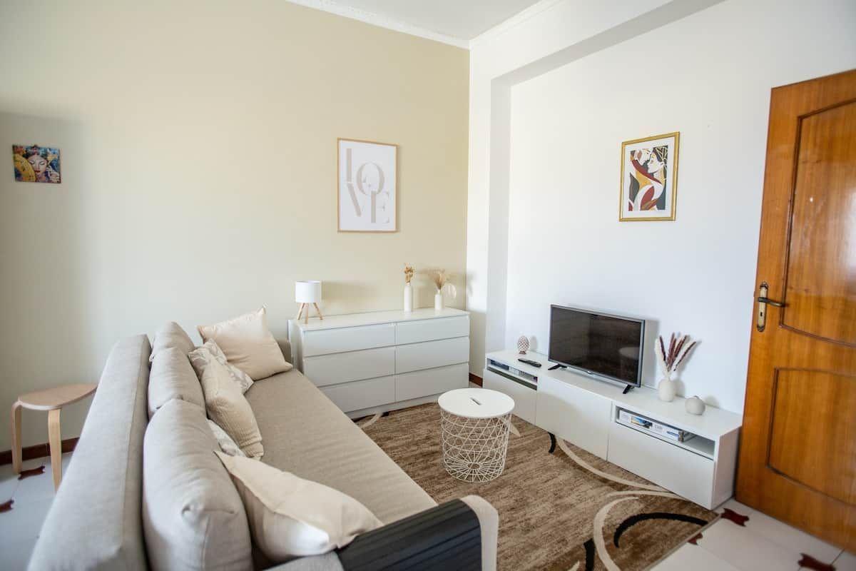 En moderne stue med sofa, TV, hvidt skab og billedkunst på væggene.