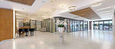 A spacious lobby with a piano, seating area, and a central decorative table.