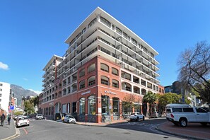 A multi-story hotel with a prominent SOFACOMPANY sign, a parking lot, and a street view with cars and pedestrians. - Stylish 1-Bed Apt in trendy De Waterkant with Balcony (Cape Town)