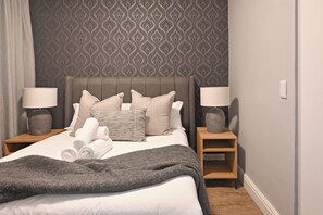 A neatly made bed with pillows and a blanket, two bedside lamps, and a patterned wallpaper. - Stylish 1-Bed Apt in trendy De Waterkant with Balcony (Cape Town)