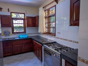 A kitchen with wooden cabinets, a gas stove, and a window with decorative glass panes. - Spacious 4-bedroom paradise villa in Diani Beach with jacuzzi and private pool (Diani Beach)