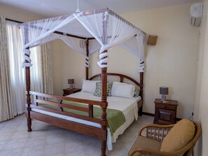 A four-poster bed with a canopy, a bedside table with a lamp, a chair, and a wall-mounted air conditioner. - Spacious 4-bedroom paradise villa in Diani Beach with jacuzzi and private pool (Diani Beach)
