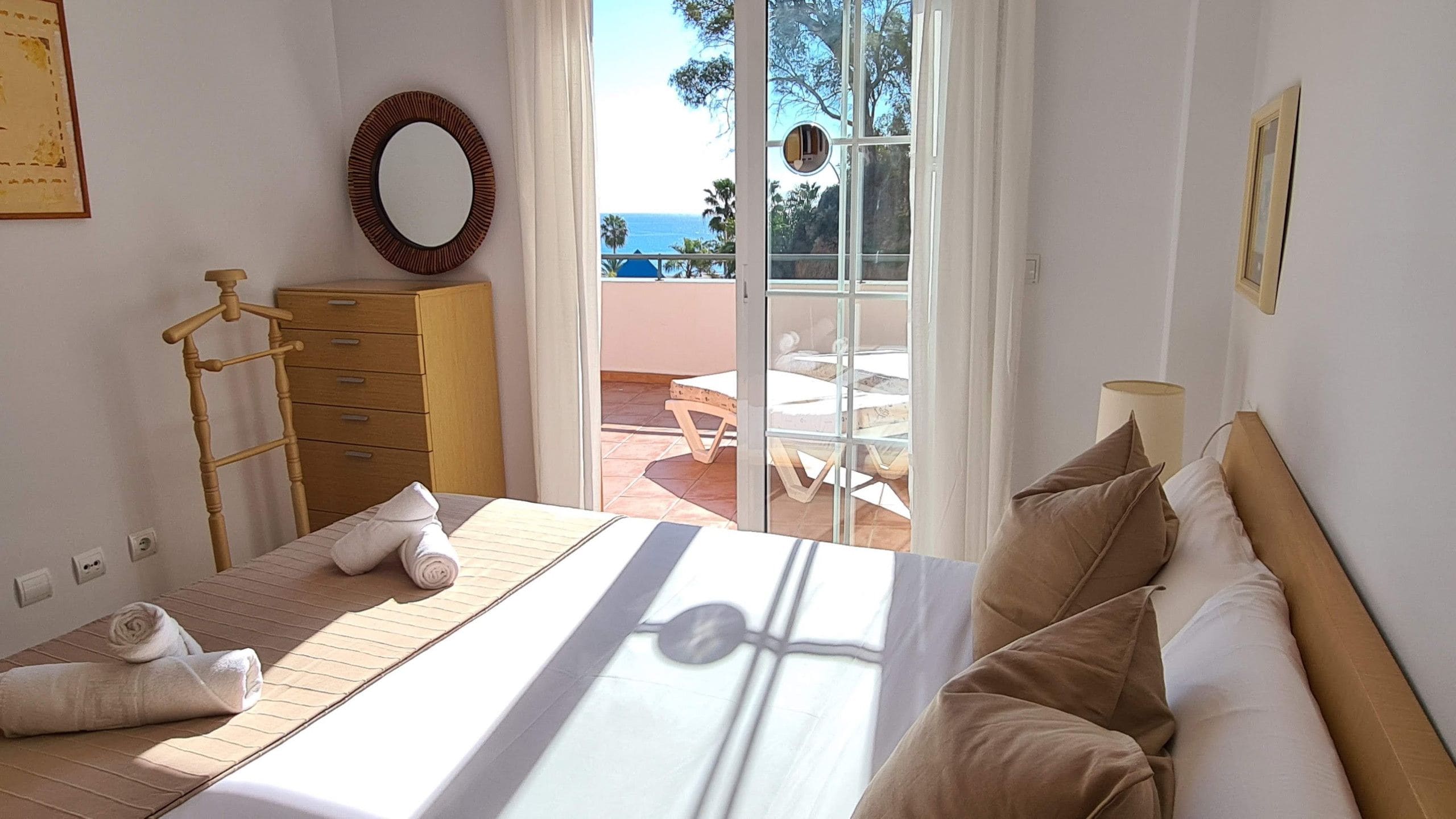 Un dormitorio con una cama, un aparador de madera, un espejo y vistas al exterior.