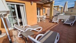 A sunlit outdoor patio with white lounge chairs, a table, and a covered seating area. - Burriana Beach Apartment (Nerja)