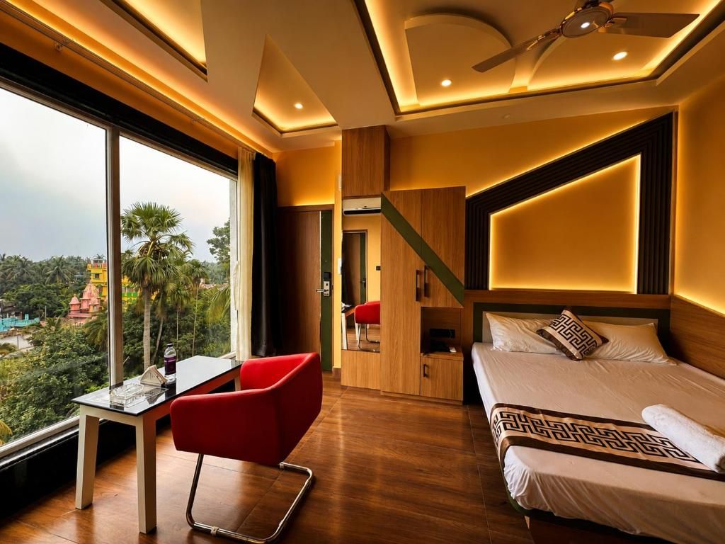 Quarto de hotel com uma cama, uma escrivaninha e uma cadeira. Uma janela grande oferece vista para o exterior.