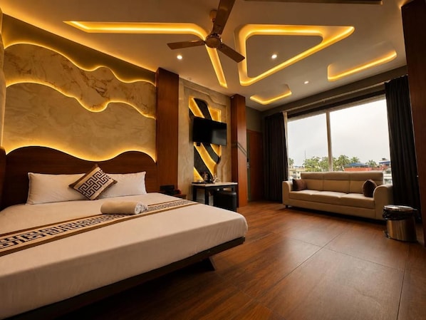 A modern hotel room with a large bed, a sofa, a ceiling fan, and a view through a large window.