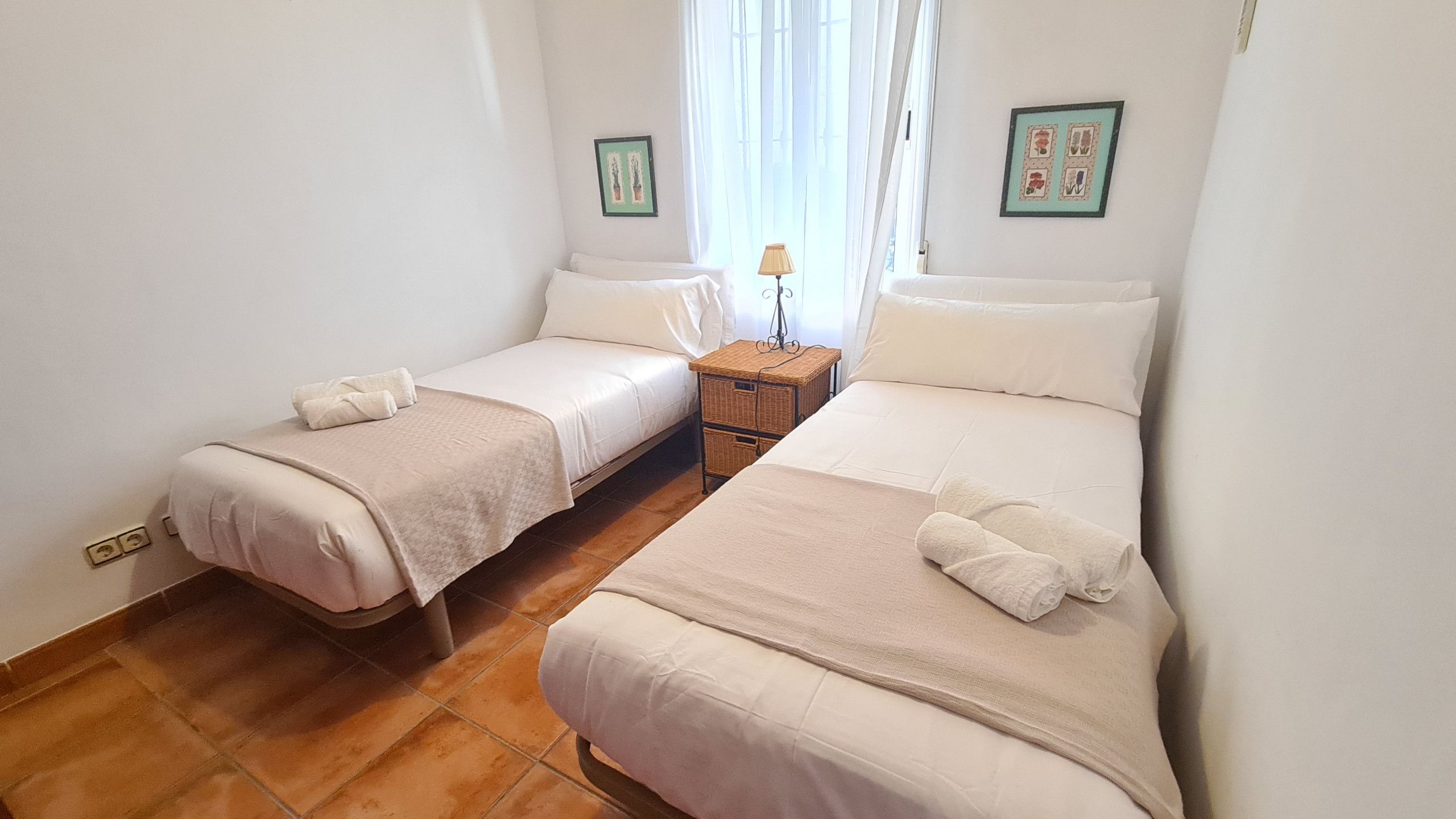 A twin room with two beds, a nightstand, a lamp, and two framed pictures on the wall.
