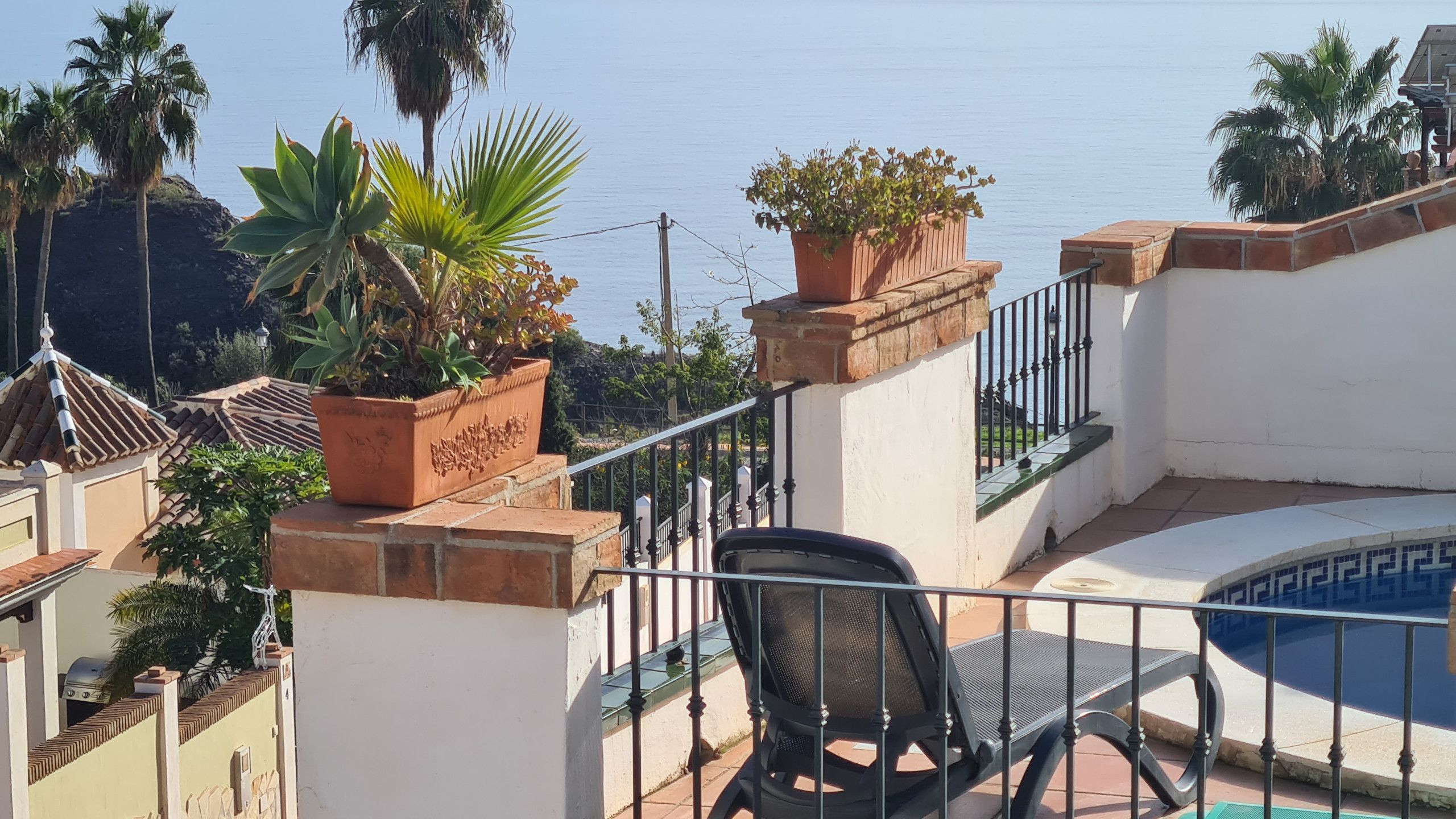 A balcony with a pool, potted plants, and a chair.
